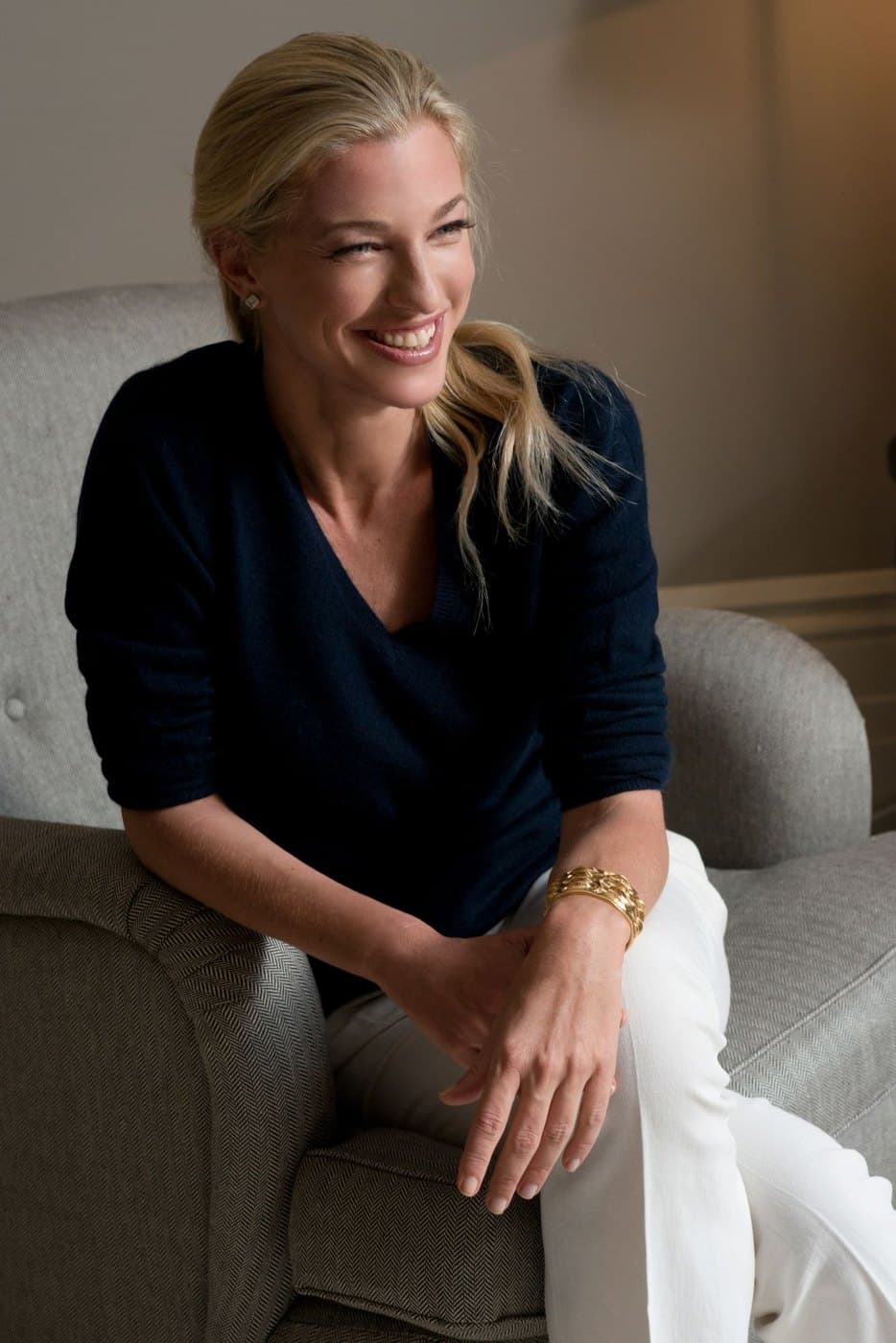 Nicole Junkermann seated in a navy jumper in a softly lit room, smiling and looking to one side